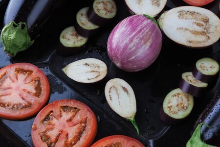 Whole and sliced eggplants and tomatoes on rustic baking tray closeup. Shallow depth of fieldの写真素材