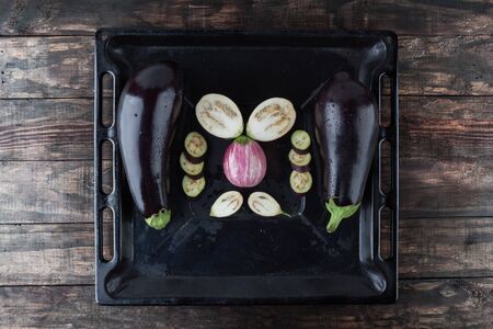Whole and sliced eggplants arranged on rustic baking tray. Top view with copy spaceの写真素材