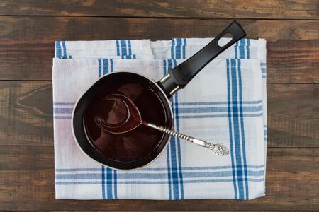 Pan filled with dark melted chocolate with vintage silver spoon on checkered napkin and wooden table. Top viewの写真素材