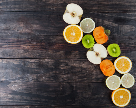 Slices of healthy fruits on dark rustic wooden table. Apple, orange, lemon, kiwi and persimmon. Top...