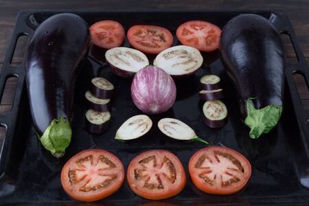 Whole and sliced eggplants and tomatoes on rustic baking tray. Shallow depth of fieldの写真素材