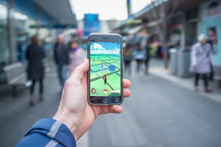 Melbourne, Australia - August 12, 2016: Male hand holding iPhone 6 with Pokemon Go game  on a busy streetのeditorial素材