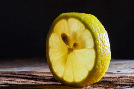 Closeup of slice of lemon glowing with back translucent light on rough wooden surfaceの写真素材