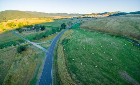 Aerial panorama of Australian countryside at sunset. Hay bales scattered on a green field near the...