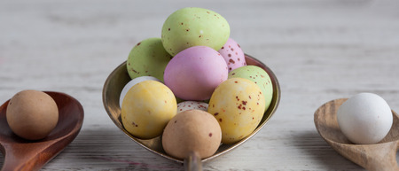 Easter eggs - speckled and sugar coated on wooden and silver spoons on white rustic wooden table. Closeup with shallow depth of fieldの写真素材