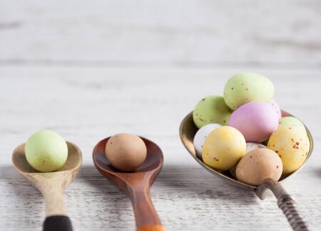 Easter eggs - speckled and sugar coated on wooden and silver spoons on white rustic wooden table. Closeup with shallow depth of field. Square image with copy spaceの写真素材