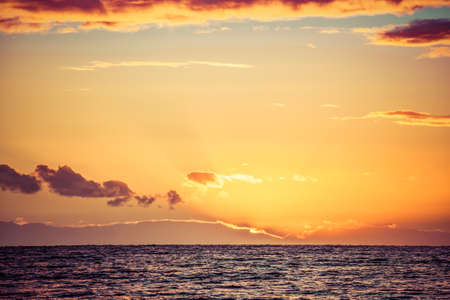 Clouds and sky glowing in orange at sunset over sea. Nothing but sky and waterの写真素材