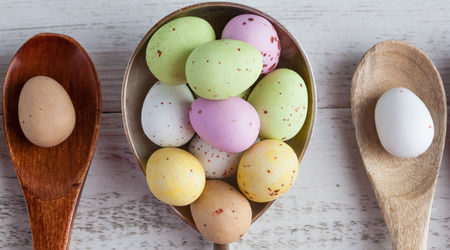 Easter eggs - speckled and sugar coated on wooden and silver spoons on white rustic wooden table, top view extreme closeupの写真素材