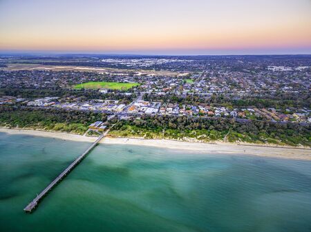 Aerial view of long wooden pier stretching into shallow ocean water and coastal suburban houses in Melbourne, Australiaの写真素材