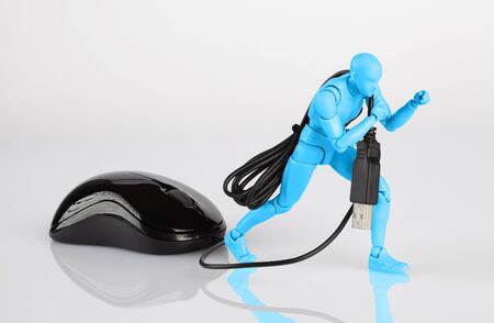 Blue male figurine dragging a computer mouse across white table. Corporate job, slavery, and debt concept with copy spaceの写真素材