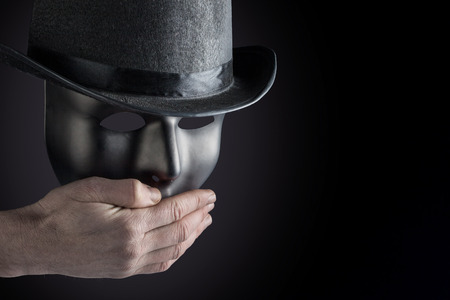 Male hand hiding mouth of black mask wearing black top hat on black background with copy space. Freedom of speech conceptの写真素材