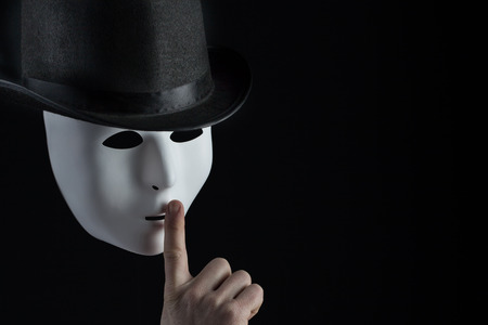 Male finger showing shh sign on white mask wearing black top hat on black background with copy space. Freedom of speech and silence conceptの写真素材