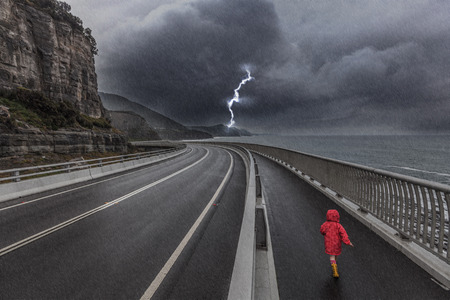 Child running on a huge bridge during thunderstorm. Concept of lonelines and dangerの写真素材
