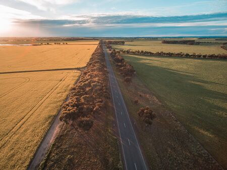 Aerial view of rural road passing through agricultural land in Australian countryside at sunsetの写真素材