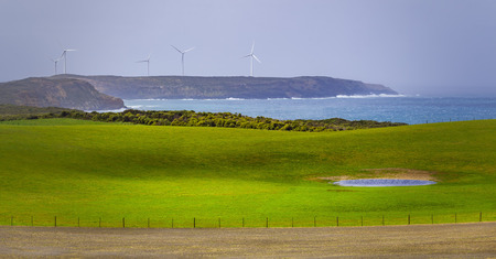 Meadows and pastures with wind turbines standing on a rugged cliff in the backgroundの写真素材
