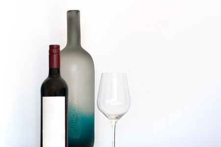 Wine bottle with empty label, wineglass and decorative frosted glass bottle on white background with copy spaceの写真素材