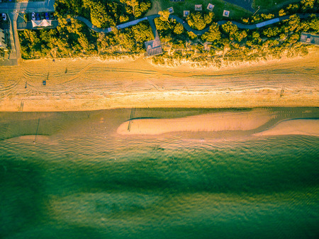 Looking down at vivid green ocean water and yellow sandy beach at sunset - aerial viewの写真素材