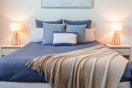 Beautiful arrangement of pillows on bed in a bedroom with bedside lamps and copy spaceの写真素材