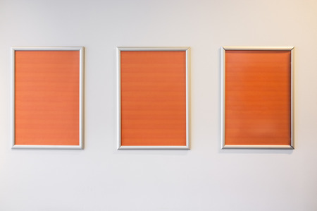 Three picture frames with orange copy space hanging on white wall