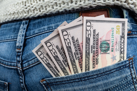 Current economy state concept - US dollar bills in back pocket of woman wearing blue jeans