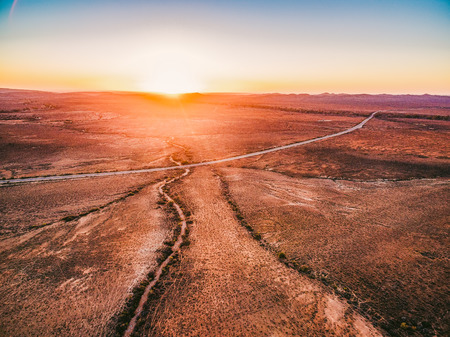 Orange sunset over dry land and rural highway passing throughの写真素材