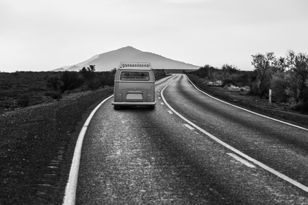 Old minivan driving on winding road leading to a scenic mountain peak in black and whiteの写真素材