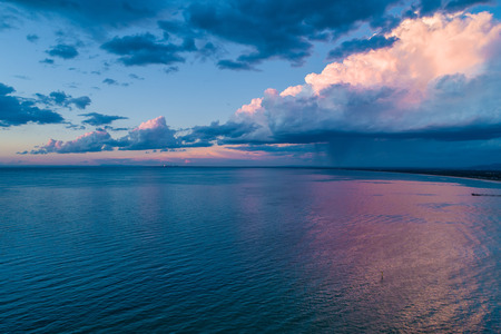 Rain and stormy clouds approaching the ocean coastline and beautiful sunset - aerial viewの写真素材