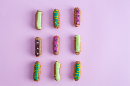 Decorative French eclairs organised in rows on pink background - top view with copy space