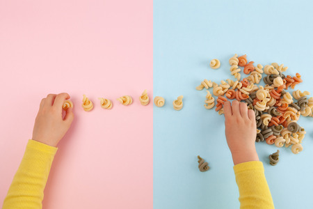 Girl's hands playing with Funghetto veggie pasta on colored table with copy spaceの写真素材