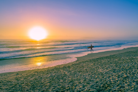 Surfer silhouette walking on ocean beach at sunset