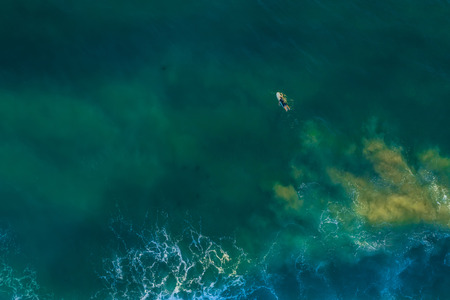 Lonely surfer lying on surfboard in vast ocean - aerial view with copy spaceの写真素材