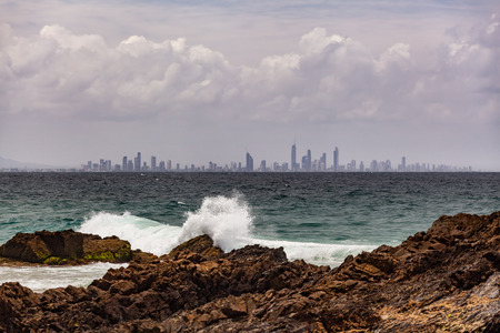Ocean waves crushing on Snapper Rocks with Gold Coast City skyline in the backgroundの写真素材