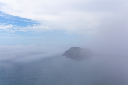 Low clouds and mist over ocean concealing a small island - mystical landscapeの写真素材