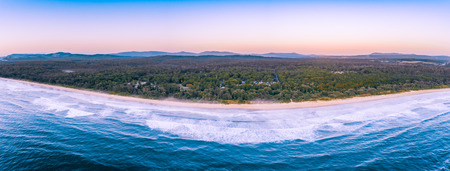 Aerial panorama of ocean waves washing up the coastline and coastal vegetation with mountains in the background in the morning with copy spaceの写真素材
