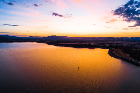 Lone boat sailing across scenic lake at vivid orange sunset - aerial viewの写真素材