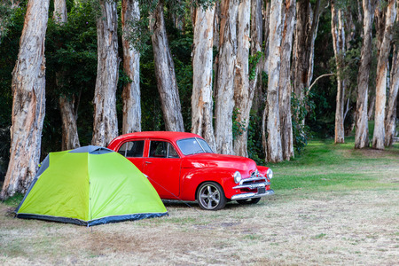 Red vintage car parked next to a small tent on green grass under treesの写真素材