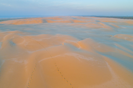 Footprints across sand dunes glowing in orange sunrise - aerial view. Anna Bay, New South Wales, Australiaの写真素材
