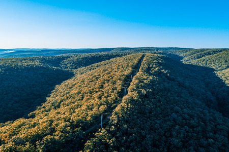 Aerial view of power lines among forested hills at sunrise in Australiaの写真素材