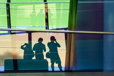 People taking pictures silhouettes reflecting in tall windows of modern building