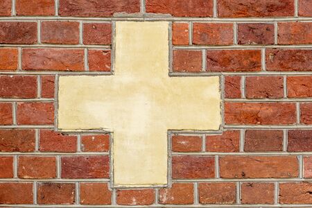 Red brick wall with white-yellowish cross sign backgroundの写真素材