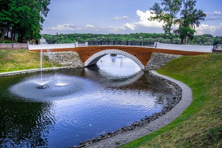 Swan pond with fountain and red footbridge in the city park of Gomel, Belarusの写真素材