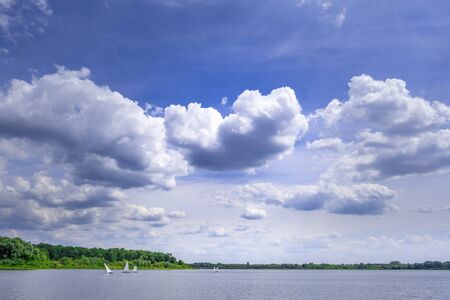Sailboats sailing on a river under beautiful sky with white fluffy cloudsの写真素材