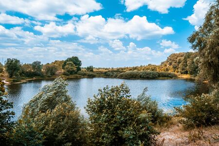 Countryside landscape of river, trees and white fluffy clouds in blue skyの写真素材