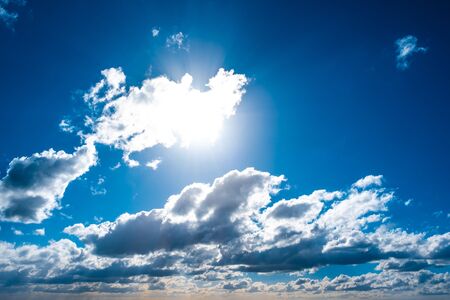 Blue sky with sun shining through white clouds background overlayの写真素材