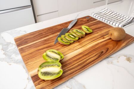 Whole and sliced kiwi fruit on wooden cutting board with knife in modern kitchenの写真素材