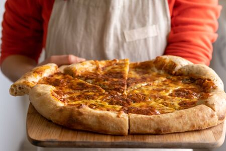 Female person midsection hodling large homemade pizza on wooden trayの写真素材