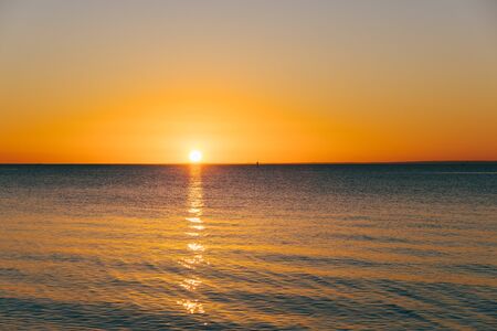 Golden sun touching the horizon over calm sea with copy spaceの写真素材