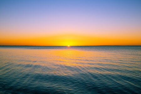 Vivid beautiful sunset - sun almost disappeard behind the horizon over calm sea with copy spaceの写真素材
