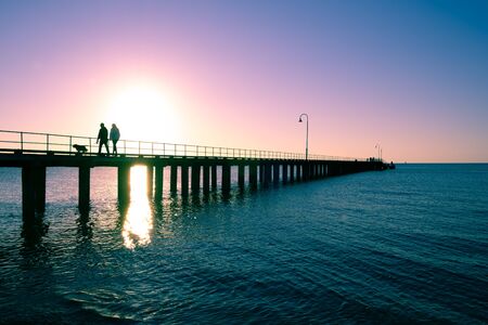 Couple with dog silhouettes on wooden pier at sunsetの写真素材