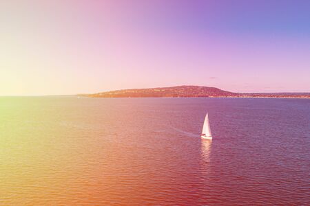 White sailboat sailing across Port Phillip Bay at sunset. Melbourne, Australiaの写真素材